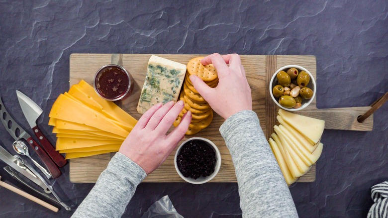 Hands arranging crackers and cheese on a charcuterie board.