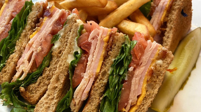 A turkey club cut into triangles and served with french Fries and a pickle.