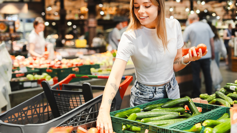 A woman in a grocery store reaches for tomatoes in the produce section