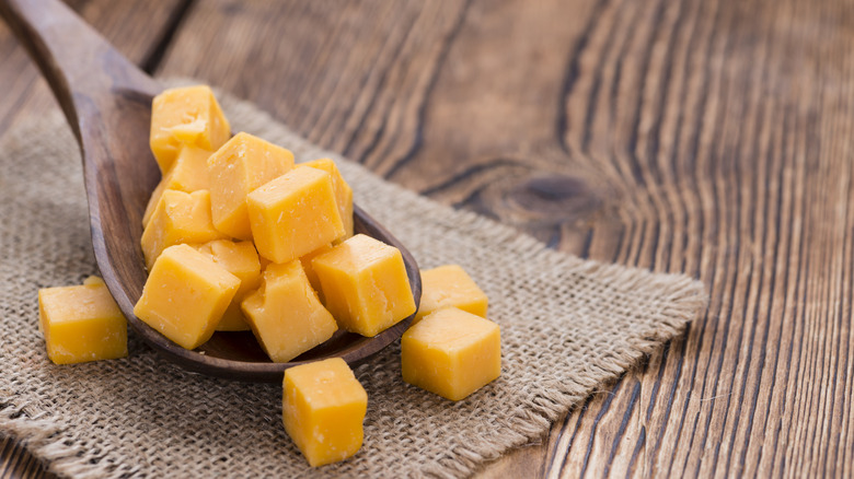 Diced cheddar cheese spills from a wooden spoon.