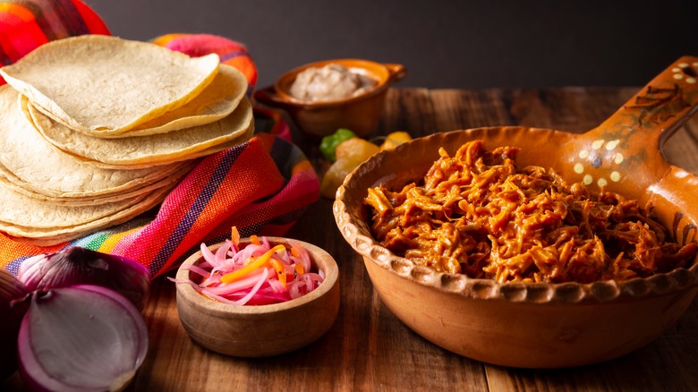 A bowl of cochinita pibil with pickled onions and tortillas