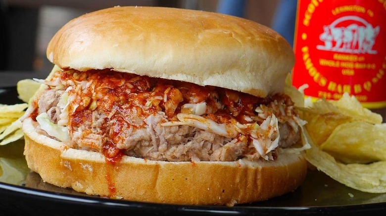 A pulled pork sandwich on a plate with potato chips from B.E. Scott's BBQ