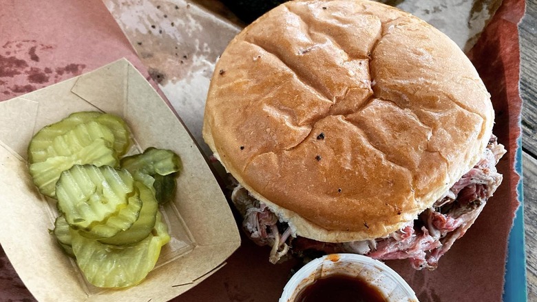 A pulled pork sandwich with a side of pickles from Franklin Barbecue