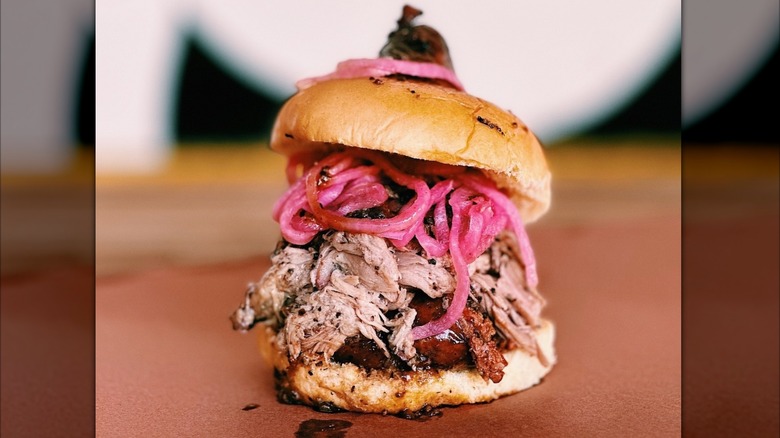 A sandwich with pulled pork, brisket, sausage, and pickled onions from La Barbecue