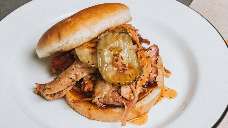 A pulled pork sandwich with pickles on a plate from Saw's BBQ