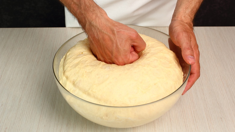 A hand punching over-proofed dough