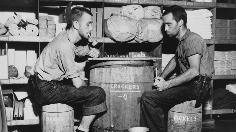 Two men sit at a barrel of soda crackers.