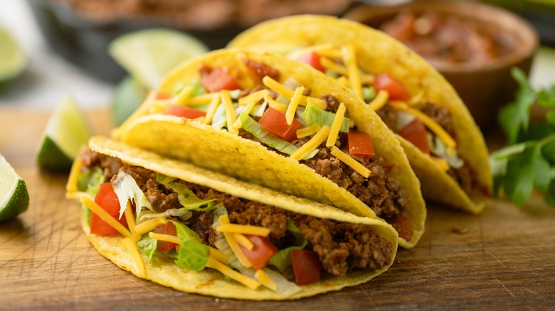 Three hardshell tacos on a cutting board