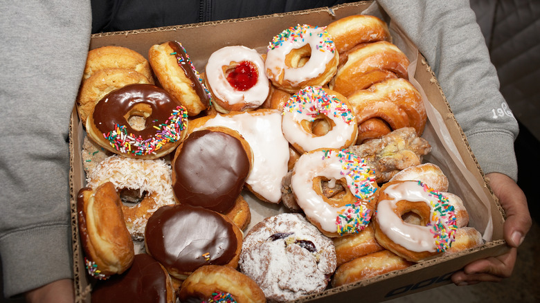 a man holds a large box of a variety of donuts