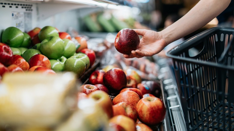 A person is picking an apple from a grocery store shelf.