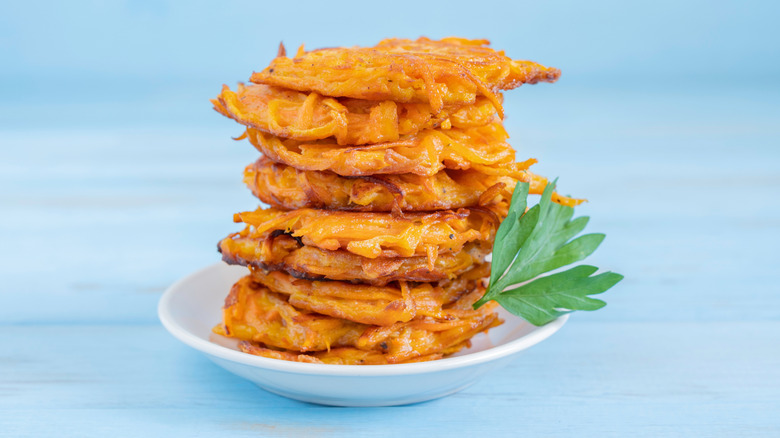 A stack of sweet potato latkes sits on a plate with a light blue background.