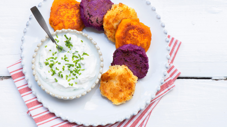 Colorful sweet potato latkes are displayed on a plate with sauce.