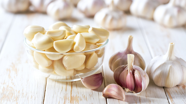 Peeled garlic cloves in a bowl next to whole garlic bulbs