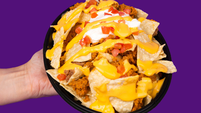 Person holding Taco Bell nachos with cheese, sour cream, seasoned beef, and tomatoes