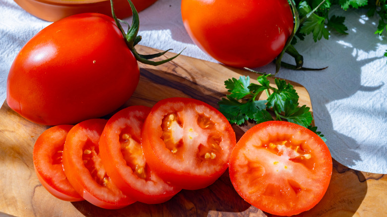 Slices of ripe roma tomatoes next to a whole tomato on a cutting board