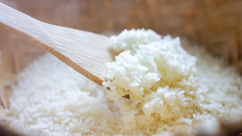 Cooked white rice in a bowl being stirred by a wooden spoon