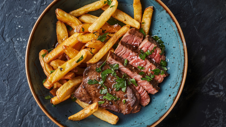 Steak frites are displayed with herbs and salt.