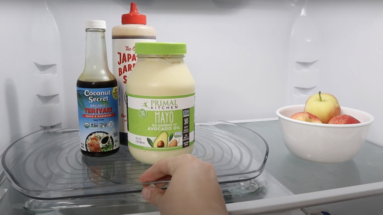 A clear plastic lazy susan in a refrigerator with bottles of condiments on top.