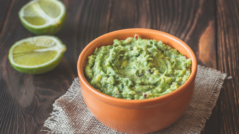 Bowl of guacamole on a wooden table with halved limes