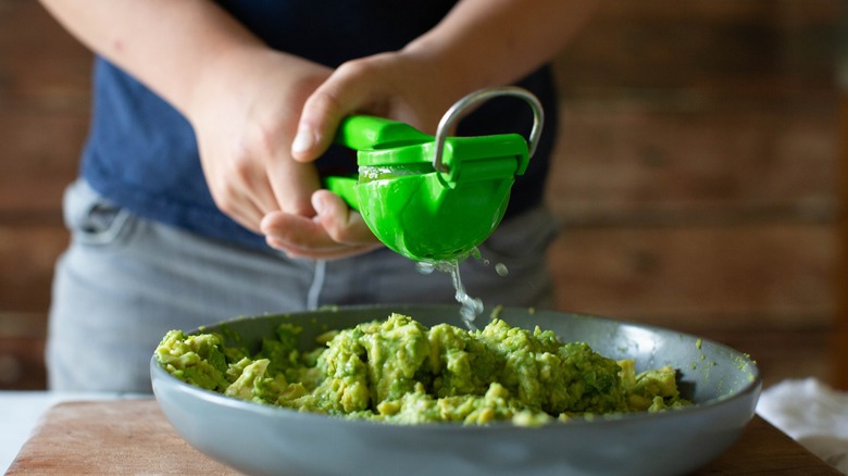 Hands using citrus juicer to squeeze lime juice on bowl of guacamole