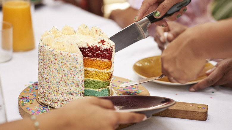 A five-tiered cake with different colored layers being sliced.