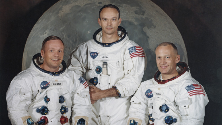 Apollo 11 astronauts pose in front of an image of the moon