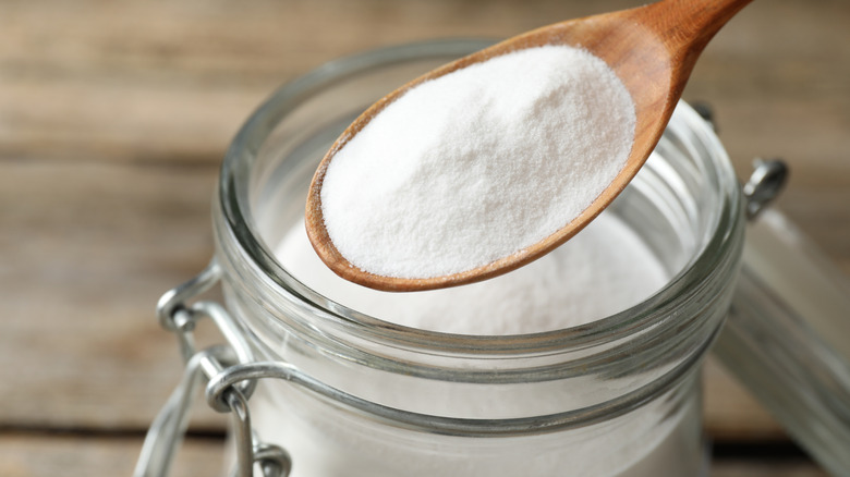 a wooden spoon holds a scoop of baking soda above a glass jar