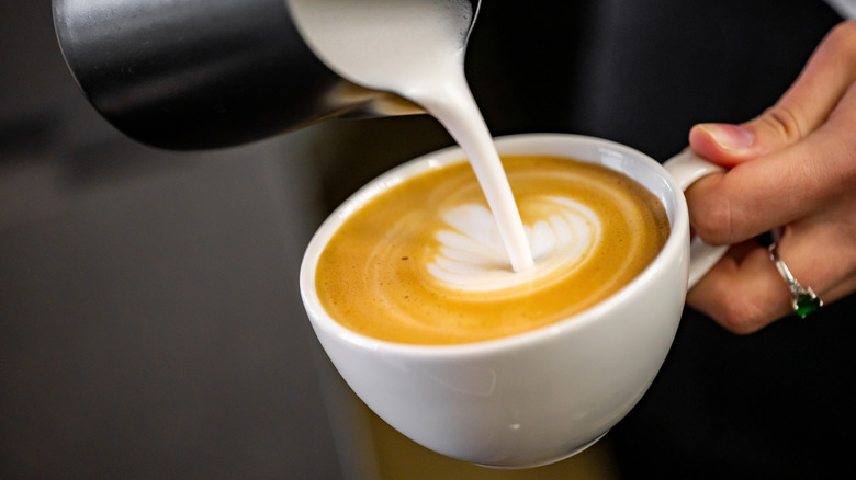 A close-up of a barista creating a design with steamed milk pouring into a coffee mug.