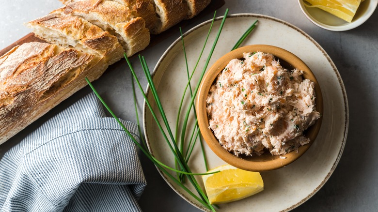 Smoked salmon dip in a bowl beside a sliced baguette.