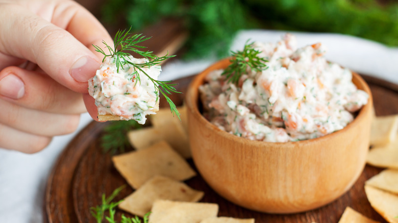 A person dips a cracker into a bowl of smoked salmon dip.