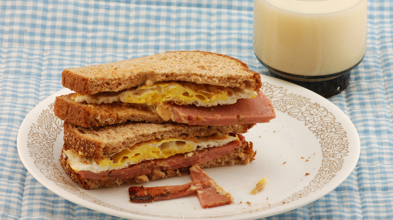 Fried bologna sandwich with fried egg on wheat sandwich bread next to a glass of milk