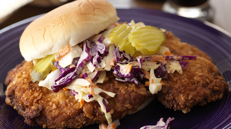 Fried pork tenderloin sandwich with coleslaw and pickles on a bun