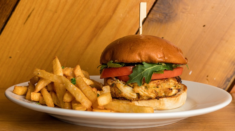 Crab cake sandwich with sliced tomatoes and arugula, and fries on a plate.