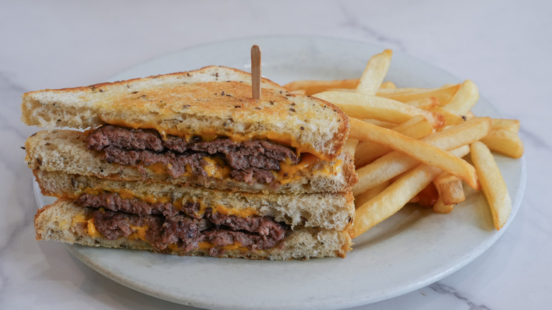 Patty melt on rye with fries on a white plate