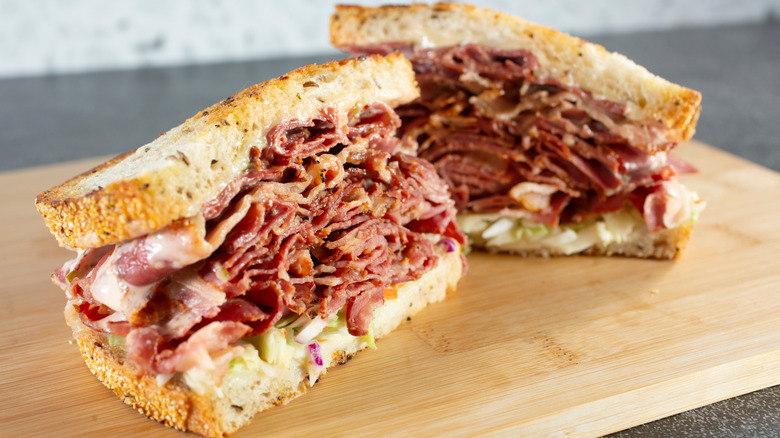 Two halves of a pastrami on rye sandwich on a wooden board