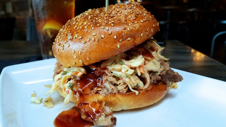 Pulled pork with BBQ sauce on a sesame seed bun on a white plate