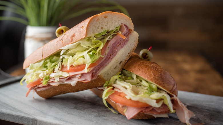 Two halves of an Italian grinder, each with a toothpick stuck through an olive