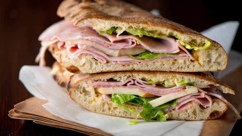 Country ham with cheese and lettuce on bread, on top of white and brown paper