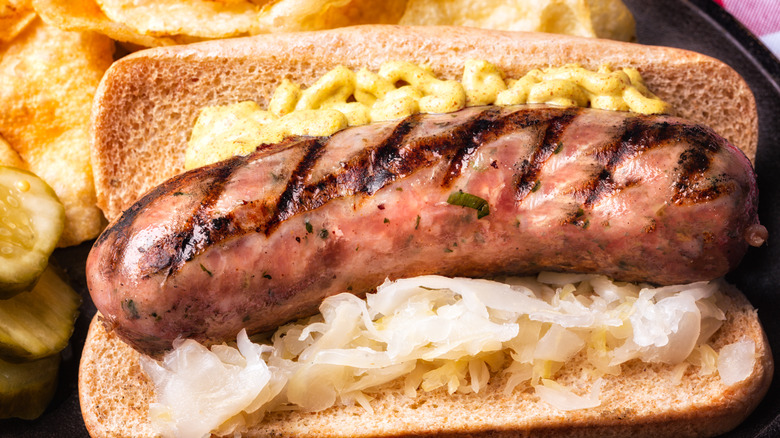 Bratwurst on bun with sauerkraut and mustard, with potato chips on a black plate