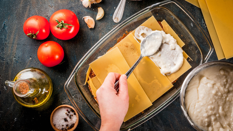 A person's hand is seen assembling a lasagna from above.
