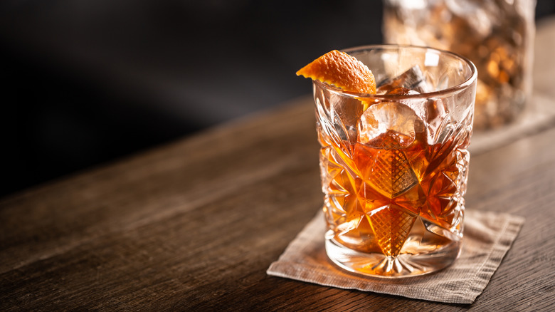 An Old Fashioned cocktail with an orange peel in a faceted glass