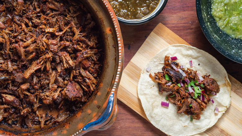 pork carnitas taco on cutting board next to large pot of carnitas