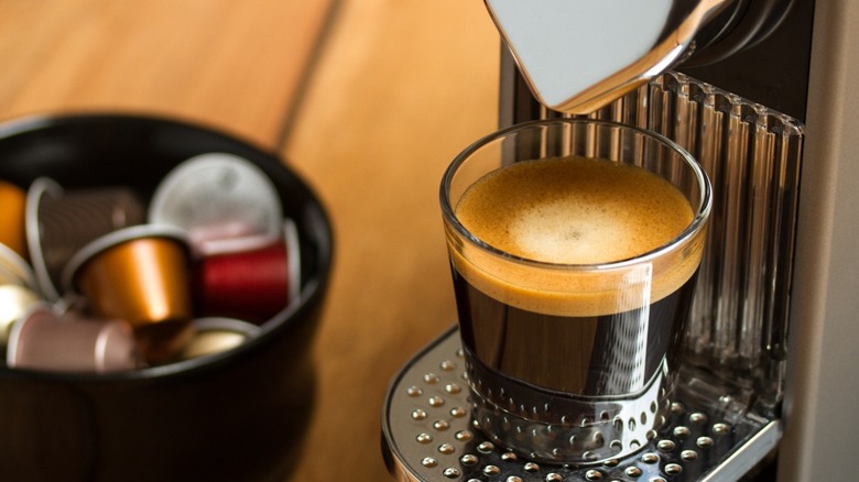 Nespresso machine dispensing espresso next to coffee pods