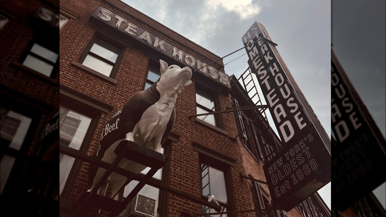 Exterior shot of Old Homestead Steakhouse's sign, brick facade, and cow statue