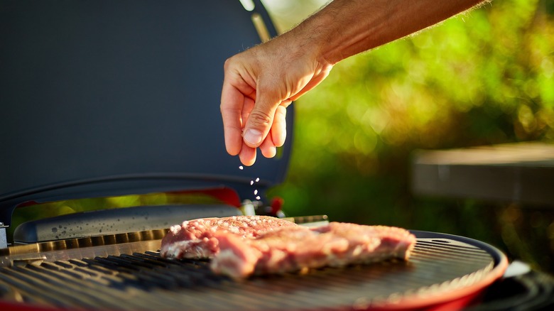 Man seasoning steak on grill