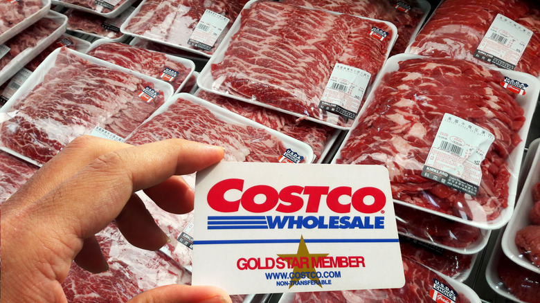 Person holding Costco card above Kirkland Signature packaged meat