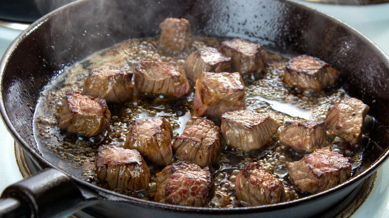 Cubes of beef searing in a pan on a stovetop.