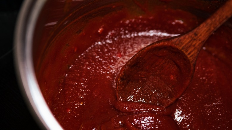 Wooden spoon stirs barbecue sauce in a pot
