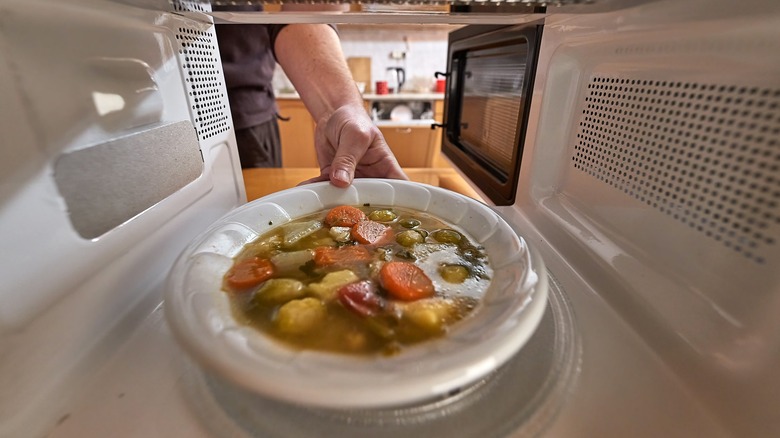 Hand putting soup in microwave