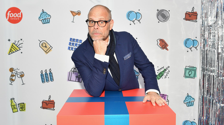 Alton Brown stands at a podium in front of a Food Network backdrop